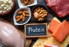 An assortment of protein-rich foods including grilled chicken, salmon, eggs, nuts, and cheese on a wooden platter.