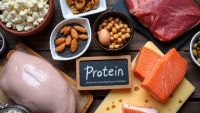 An assortment of protein-rich foods including grilled chicken, salmon, eggs, nuts, and cheese on a wooden platter.